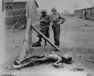 Two American soldiers conducting an investigation of a sub-camp of Buchenwald. They make notes while examining a corpse lying near a barbed wire fence.